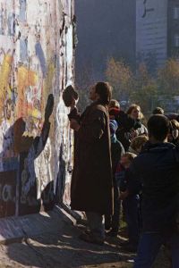 Mann steht mit einem Stein vor der Berliner Mauer